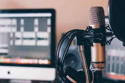 Eine Szene aus einem Tonstudio. Im Vordergrund ist ein Mikrofon zu sehen, dahinter ein Bildschirm.