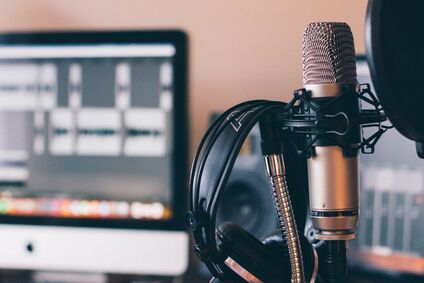 Eine Szene aus einem Tonstudio. Im Vordergrund ist ein Mikrofon zu sehen, dahinter ein Bildschirm.